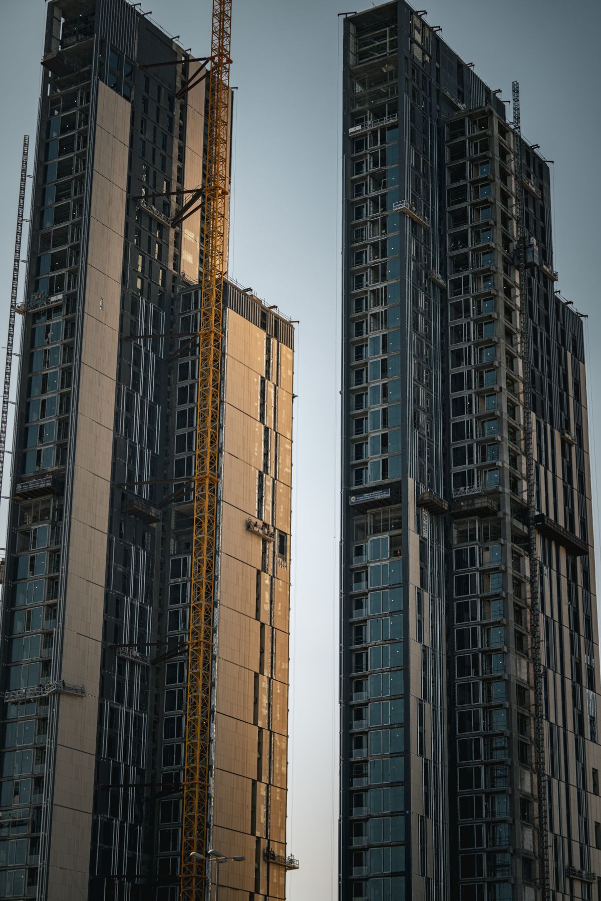 Two commercial skyscrapers under construction showing exposed structural framing and construction equipment.