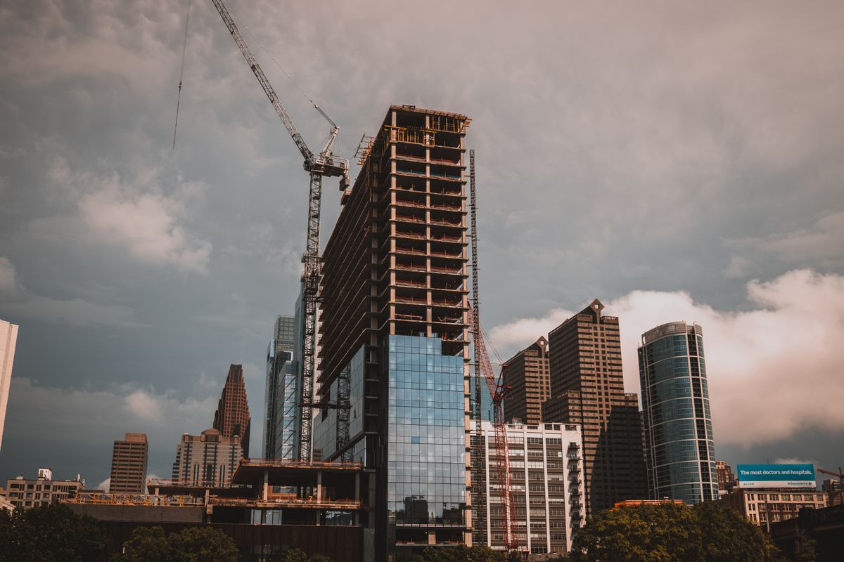 A modern high-rise commercial building under construction with tower cranes against a clear urban skyline.